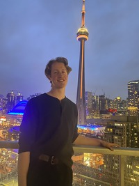Carter wearing a grey sweater standing on a balcony overlooking the CN Tower
